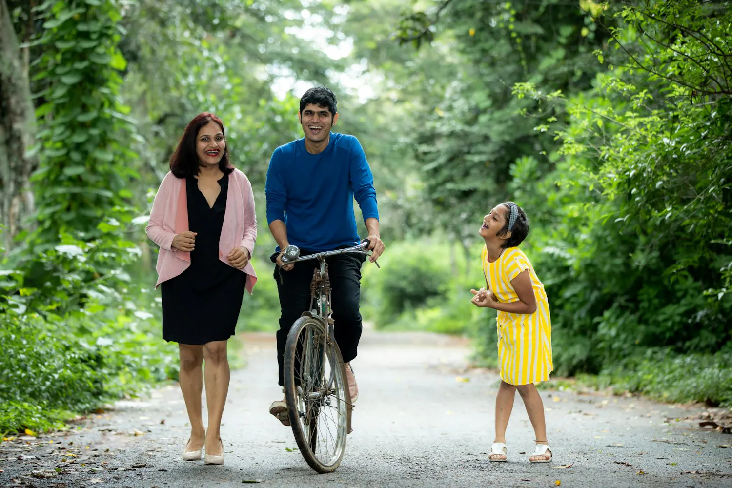 A family with a young child enjoying a lush, green tree-lined path together.